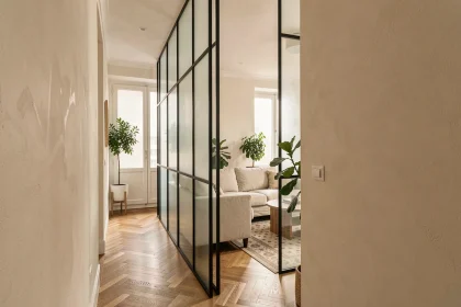 Verrière intérieure en acier noir séparant un couloir et un salon dans un petit appartement parisien avec parquet en chêne